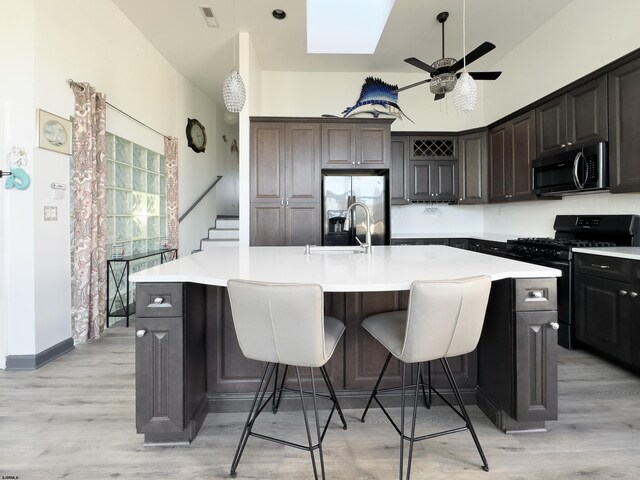 kitchen with dark brown cabinets, light hardwood / wood-style flooring, appliances with stainless steel finishes, an island with sink, and backsplash