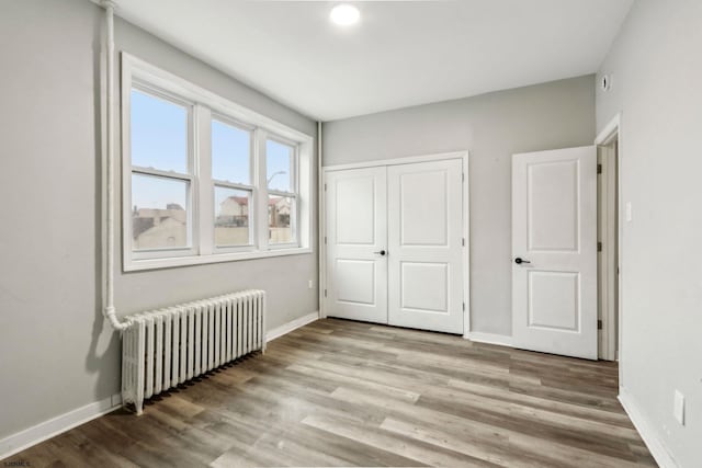 unfurnished bedroom with wood-type flooring, radiator, and a closet