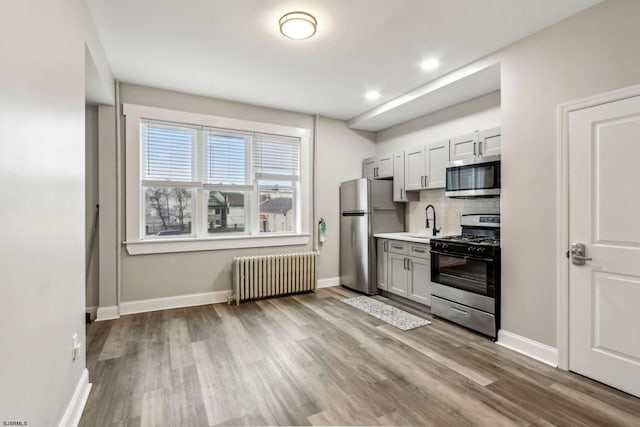 kitchen with radiator, sink, appliances with stainless steel finishes, white cabinetry, and decorative backsplash