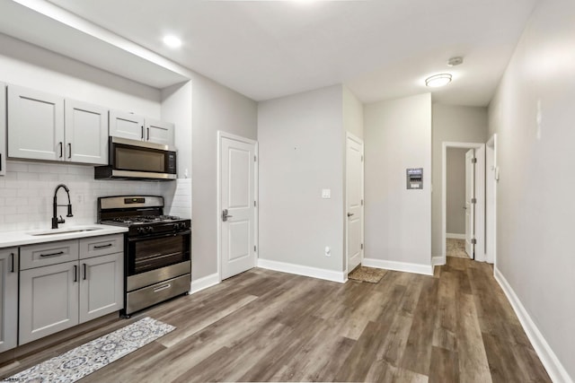 kitchen with sink, gray cabinets, dark wood-type flooring, backsplash, and stainless steel appliances