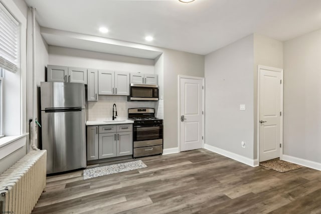 kitchen with dark hardwood / wood-style floors, radiator heating unit, gray cabinetry, backsplash, and stainless steel appliances