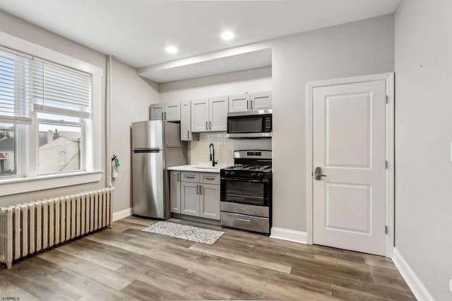 kitchen with radiator, sink, backsplash, stainless steel appliances, and light hardwood / wood-style flooring