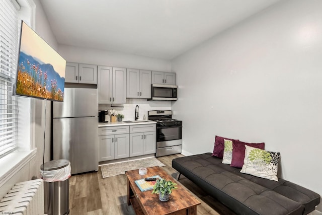 kitchen with radiator, sink, appliances with stainless steel finishes, tasteful backsplash, and wood-type flooring