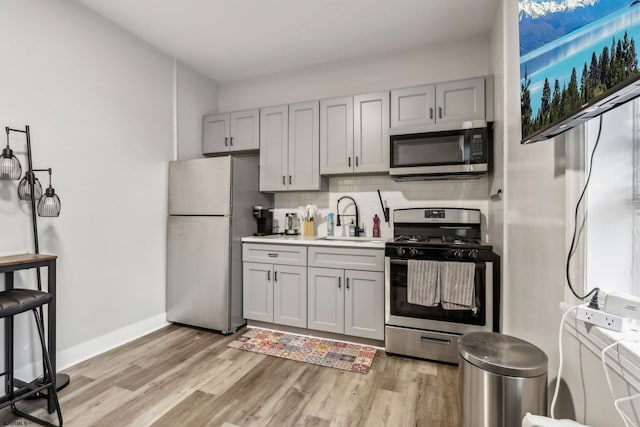 kitchen with sink, gray cabinetry, light hardwood / wood-style flooring, appliances with stainless steel finishes, and backsplash