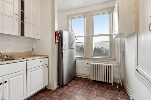 kitchen with dark parquet flooring, sink, radiator heating unit, stainless steel fridge, and white cabinets