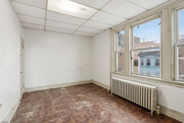 spare room with a paneled ceiling, radiator heating unit, and dark parquet floors