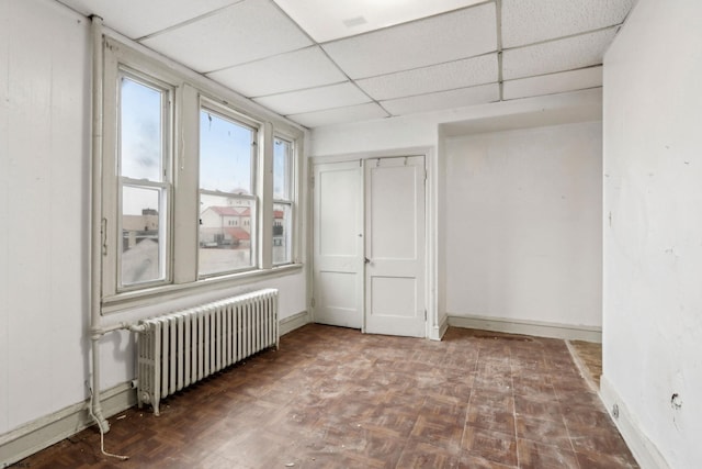 empty room featuring radiator heating unit, dark parquet floors, and a paneled ceiling