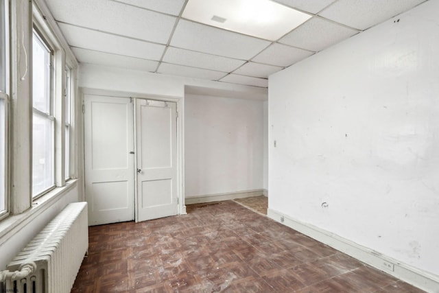 empty room with parquet flooring, radiator, a wealth of natural light, and a drop ceiling