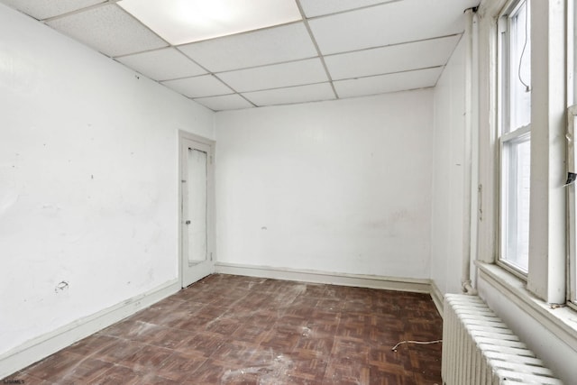 spare room with radiator, dark parquet floors, and a drop ceiling