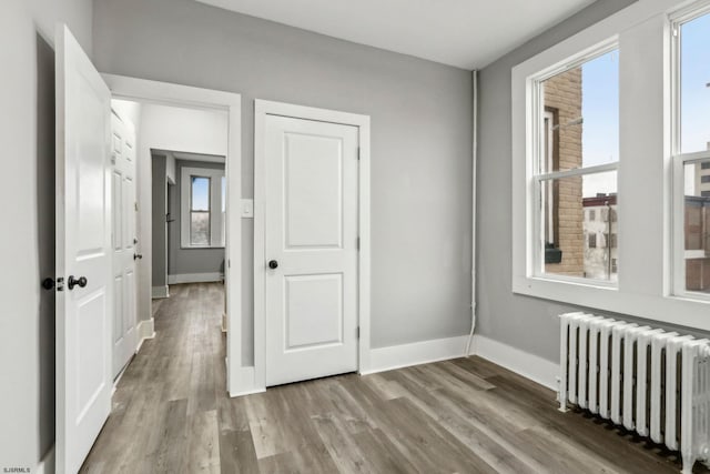 unfurnished bedroom featuring multiple windows, radiator, and hardwood / wood-style floors