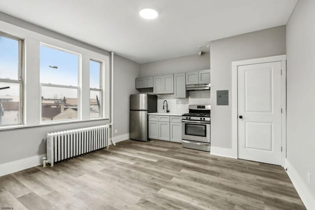 kitchen with radiator, gray cabinets, light hardwood / wood-style flooring, stainless steel appliances, and tasteful backsplash