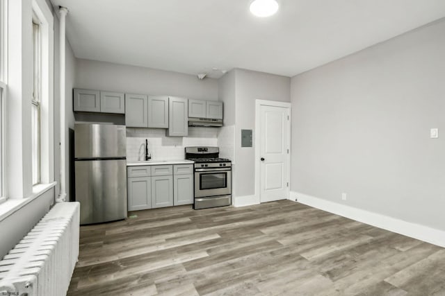 kitchen with appliances with stainless steel finishes, radiator, sink, gray cabinetry, and decorative backsplash