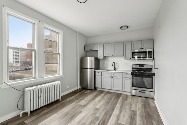 kitchen with gray cabinets, radiator heating unit, tasteful backsplash, sink, and stainless steel appliances