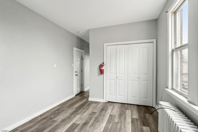 unfurnished bedroom with multiple windows, radiator, light hardwood / wood-style flooring, and a closet