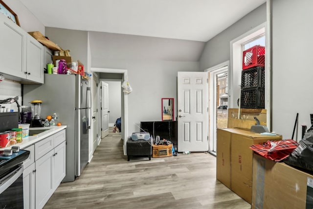 kitchen featuring appliances with stainless steel finishes, lofted ceiling, white cabinets, and light hardwood / wood-style flooring