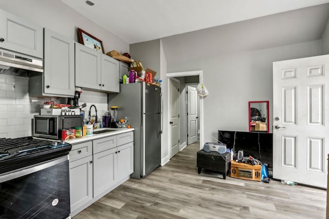 kitchen with stainless steel appliances, sink, light hardwood / wood-style floors, and decorative backsplash