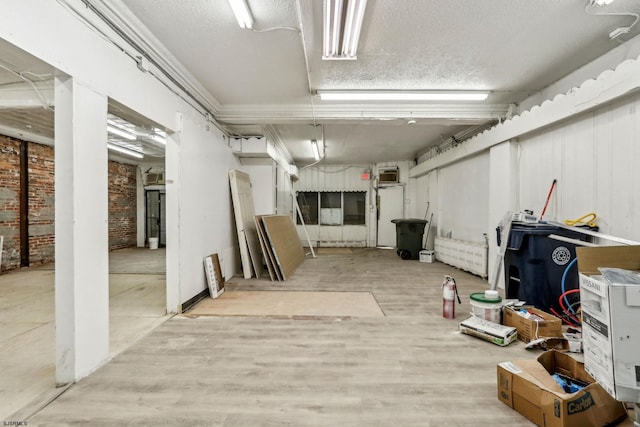 basement with brick wall, a textured ceiling, and light hardwood / wood-style floors