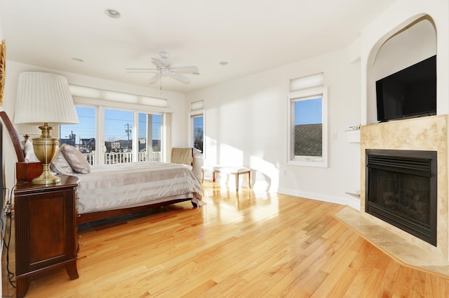 bedroom featuring a tiled fireplace, light hardwood / wood-style floors, and ceiling fan