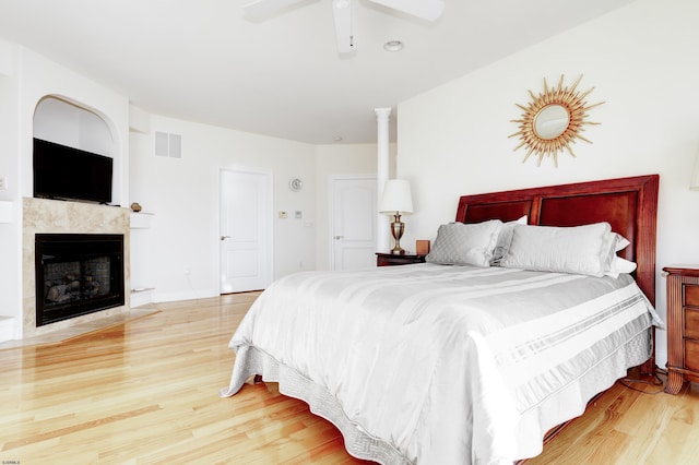 bedroom with ceiling fan, decorative columns, a tile fireplace, and light hardwood / wood-style flooring