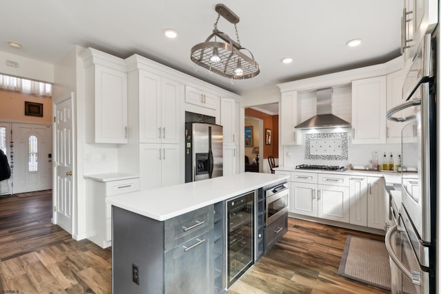 kitchen featuring appliances with stainless steel finishes, white cabinets, wine cooler, a center island, and wall chimney range hood