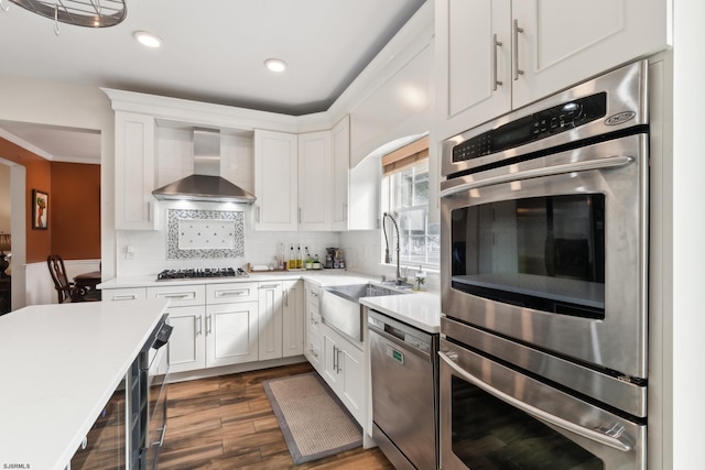 kitchen featuring appliances with stainless steel finishes, tasteful backsplash, white cabinets, dark wood-type flooring, and wall chimney range hood