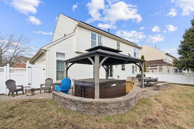 rear view of property featuring a hot tub, a gazebo, a patio area, and an outdoor fire pit