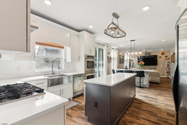 kitchen with appliances with stainless steel finishes, decorative light fixtures, sink, white cabinets, and a center island