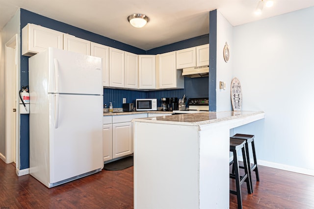 kitchen with white appliances, dark wood-type flooring, a breakfast bar, white cabinets, and kitchen peninsula