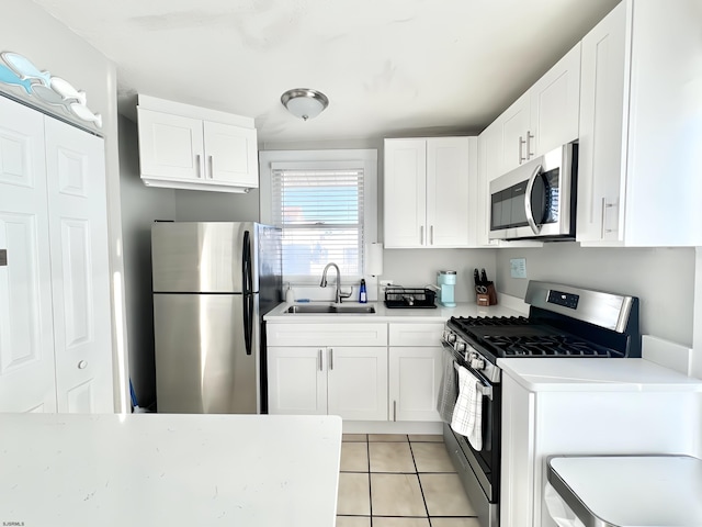 kitchen with stainless steel appliances, sink, light tile patterned floors, and white cabinets