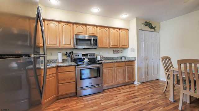 kitchen featuring appliances with stainless steel finishes, light hardwood / wood-style floors, and dark stone countertops