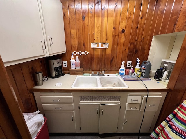 kitchen with white cabinetry, sink, and wood walls