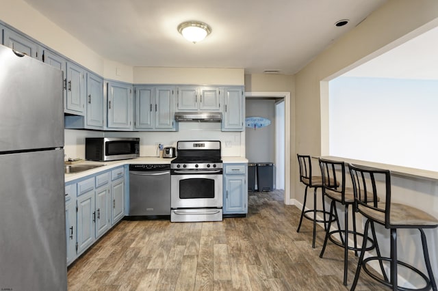 kitchen featuring wood-type flooring, appliances with stainless steel finishes, sink, and a breakfast bar