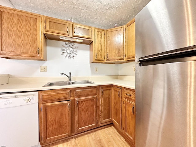 kitchen featuring sink, a textured ceiling, light wood-type flooring, stainless steel refrigerator, and white dishwasher