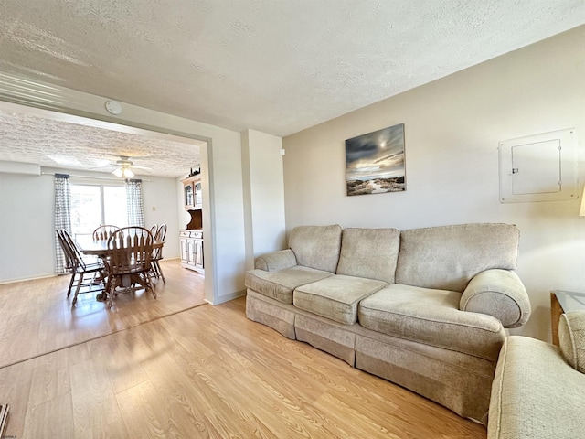 living room featuring ceiling fan, a textured ceiling, and light wood-type flooring