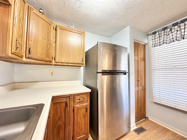 kitchen featuring sink, stainless steel refrigerator, a textured ceiling, and light wood-type flooring