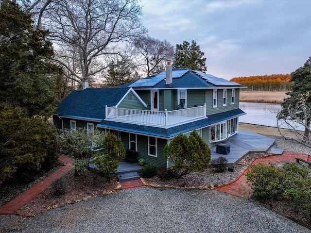 view of property with a water view, a balcony, and solar panels