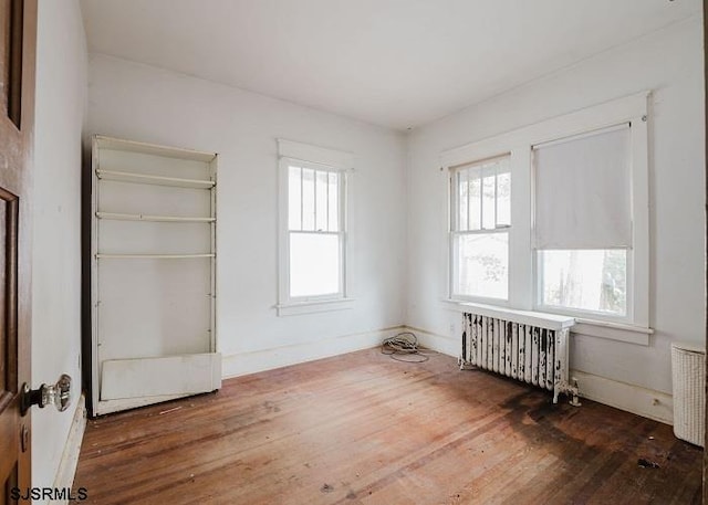 unfurnished room featuring hardwood / wood-style flooring, plenty of natural light, and radiator heating unit