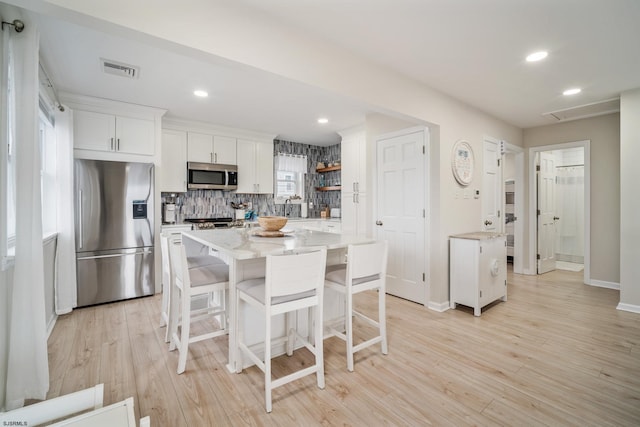 kitchen featuring appliances with stainless steel finishes, a breakfast bar, white cabinets, decorative backsplash, and light wood-type flooring