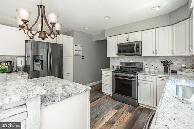 kitchen featuring tasteful backsplash, light stone counters, appliances with stainless steel finishes, pendant lighting, and white cabinets