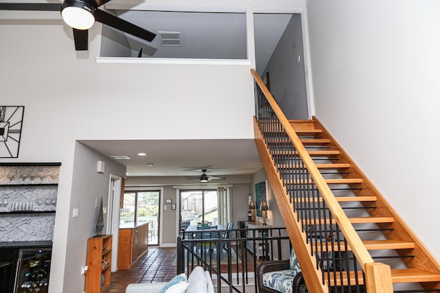 staircase featuring ceiling fan, bar, and a high ceiling