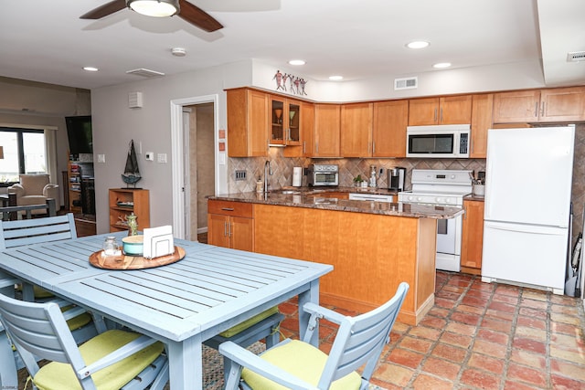 kitchen featuring sink, dark stone countertops, decorative backsplash, ceiling fan, and white appliances