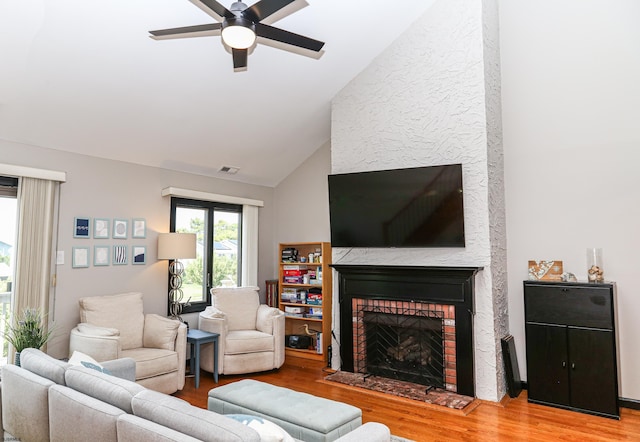 living room with ceiling fan, lofted ceiling, light wood-type flooring, and a fireplace