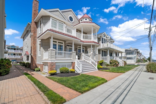 view of front facade featuring a balcony, a porch, and a front lawn