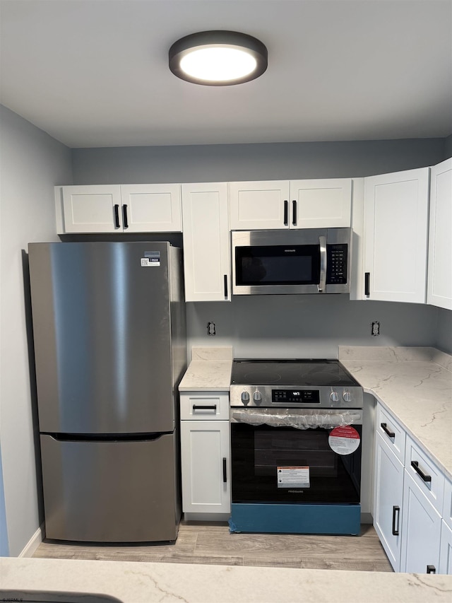 kitchen with appliances with stainless steel finishes, light stone countertops, light hardwood / wood-style floors, and white cabinets