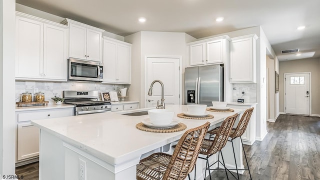 kitchen with sink, white cabinetry, a center island with sink, appliances with stainless steel finishes, and dark hardwood / wood-style flooring