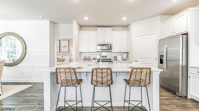 kitchen featuring sink, white cabinets, stainless steel appliances, dark wood-type flooring, and a center island with sink