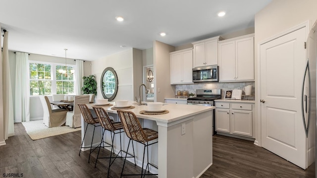 kitchen featuring white cabinetry, tasteful backsplash, decorative light fixtures, a center island with sink, and appliances with stainless steel finishes