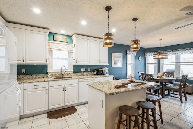 kitchen featuring sink, white cabinetry, decorative light fixtures, white dishwasher, and a kitchen island