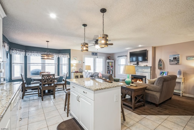 kitchen with light tile patterned floors, a breakfast bar, white cabinetry, hanging light fixtures, and light stone countertops