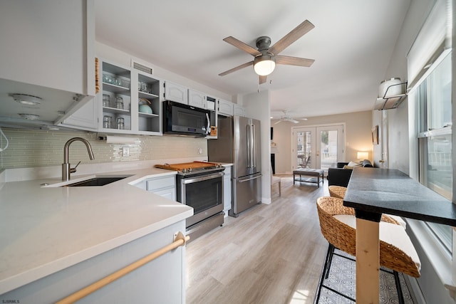 kitchen with appliances with stainless steel finishes, french doors, white cabinetry, sink, and light hardwood / wood-style flooring